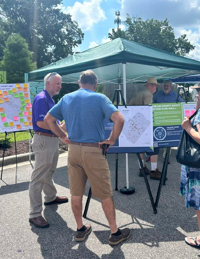 People gathered around informational displays under a tent, discussing maps and plans for safety action plan.
